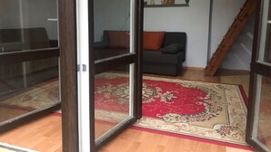 A room with a wooden floor, a red patterned rug, a dark sofa, and a staircase. - Sazava River Cottage With Boating Experience (Týnec nad Sázavou)
