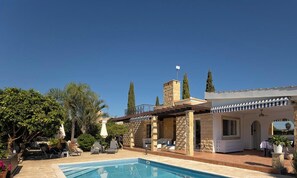 Ein Poolbereich mit Pool, Liegestühlen und einem Gebäude mit Steinmauern und einem Ziegeldach.