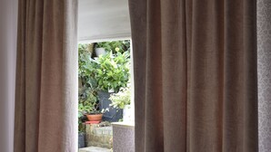 Une pièce donnant sur un espace extérieur grâce à de larges fenêtres ornées de rideaux, cet espace étant agrémenté de plantes en pot et d’un escalier.