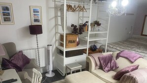 Un salon avec un canapé blanc, une petite table, un radiateur mobile et une étagère blanche agrémentée de paniers et d’objets décoratifs.