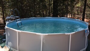 Une piscine hors sol, équipée d’une échelle et entourée de rochers et d’arbres.