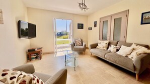 Ein Wohnzimmer mit einer Couch, einem Glastisch, einem Fernseher und einer Tür, die nach draußen führt.