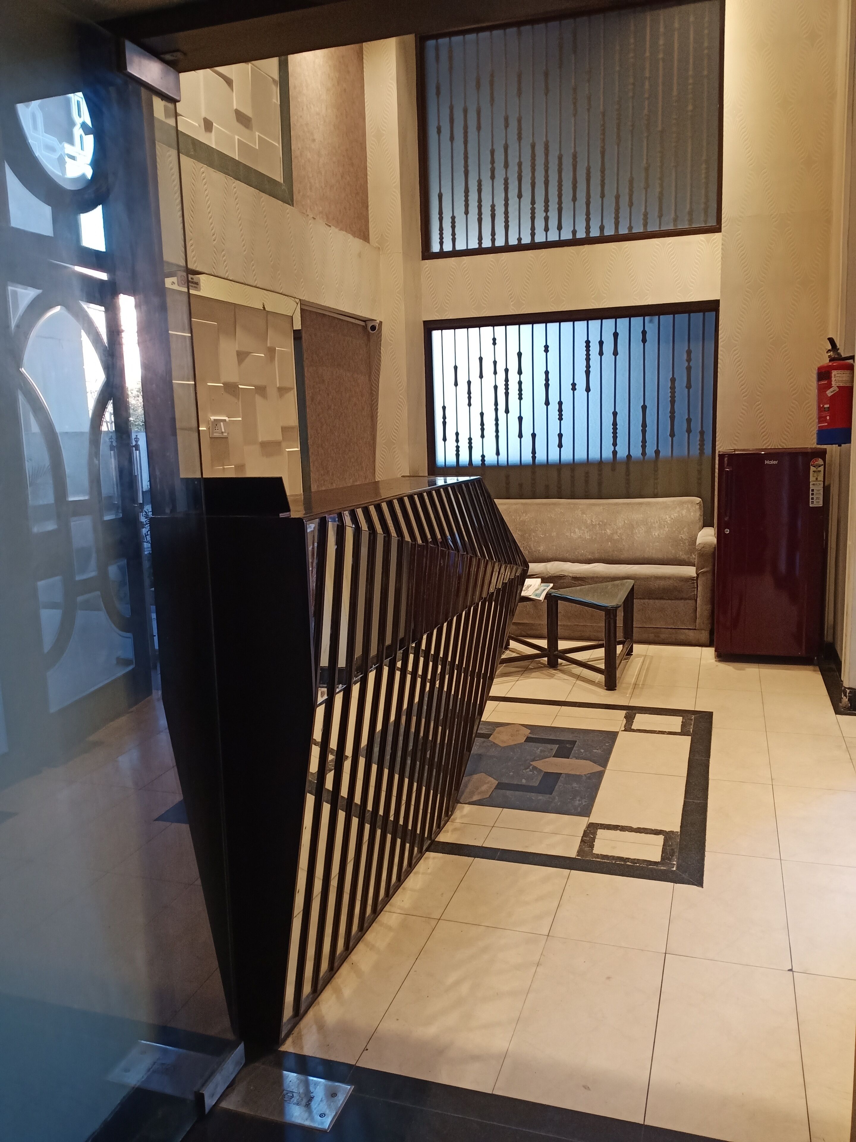 A modern lobby with a long reception desk, a sofa, a small table, and a refrigerator.