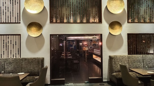 L’intérieur d’un restaurant présente un design moderne, avec une entrée principale constituée d’une porte en verre centrale, des aménagements pour les places assises et des panneaux décoratifs sur les murs.