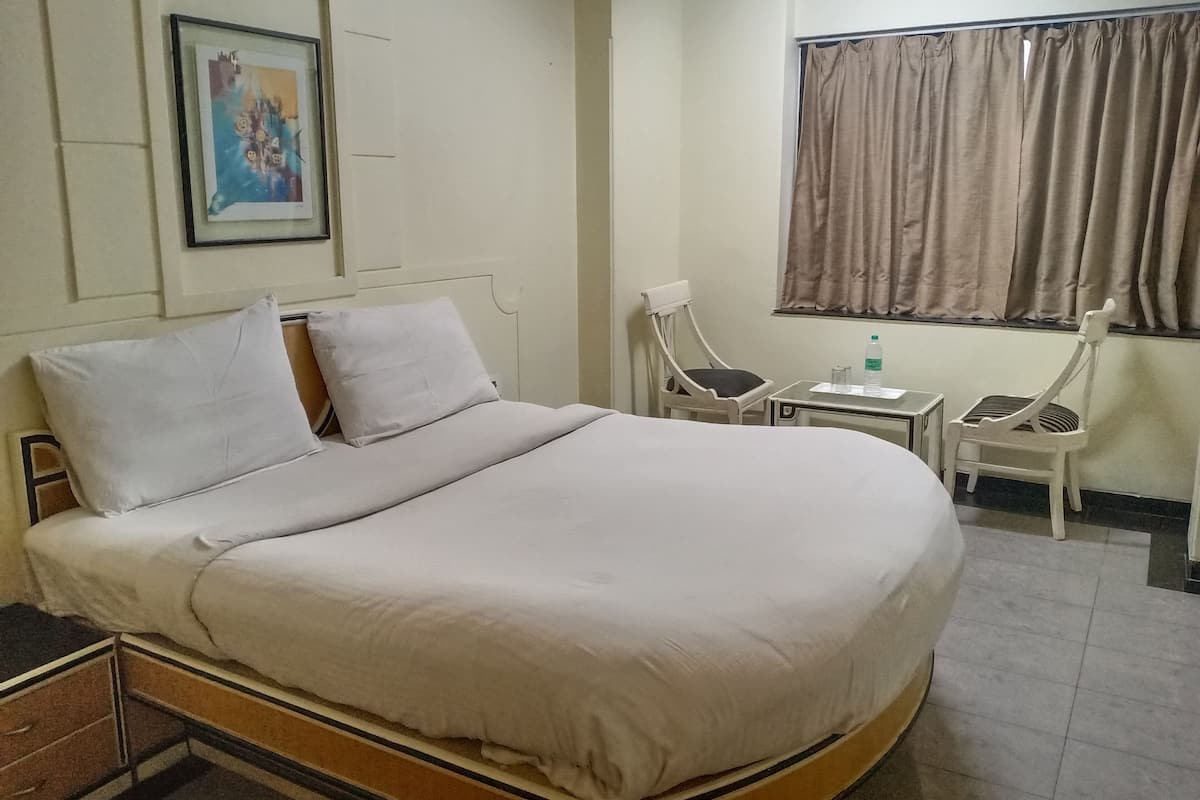 Ein Hotelzimmer mit einem großen Bett, einem kleinen Tisch, zwei Stühlen, einem Fenster mit Vorhängen und einem Bild an der Wand.