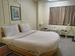 Ein Hotelzimmer mit einem großen Bett, einem kleinen Tisch, zwei Stühlen, einem Fenster mit Vorhängen und einem Bild an der Wand.