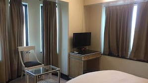 Une chambre d’hôtel avec un lit, une chaise, un bureau avec une télévision et des rideaux.