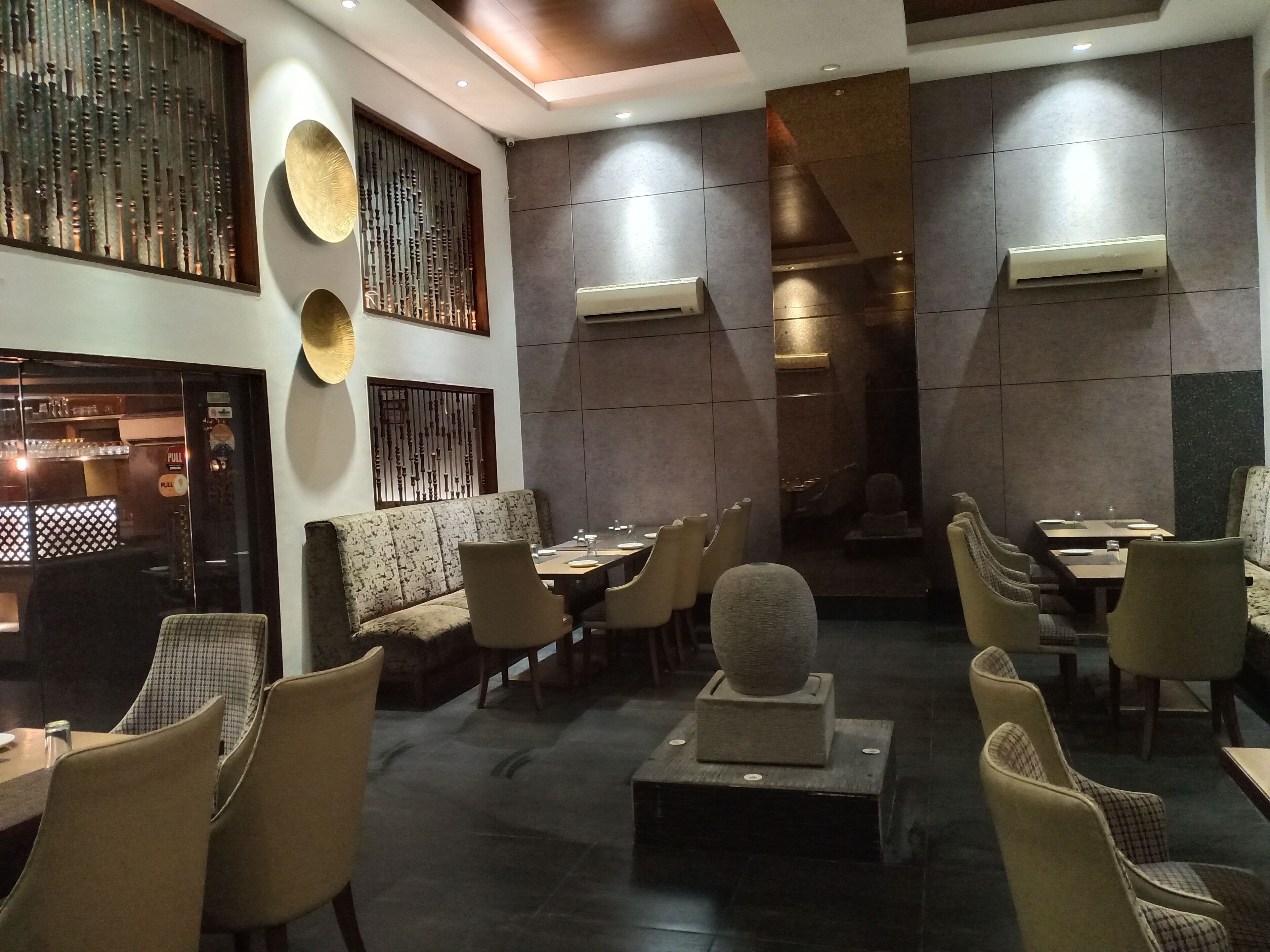 A modern restaurant interior with high tables, cushioned seating, decorative wall panels, and recessed lighting.