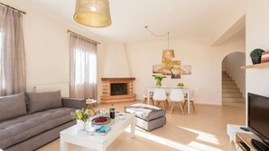 A modern living room with a sofa, coffee table, fireplace, dining area, and TV. - Peaceful Villa with Private Pool, BBQ & Kids Area (Rethymno)
