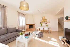 A modern living room with a sofa, coffee table, fireplace, dining area, and TV.