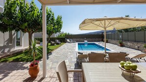 A poolside area with a table, chairs, and an umbrella. - Peaceful Villa with Private Pool, BBQ & Kids Area (Rethymno)