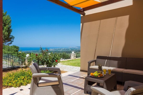 Eine Terrasse mit Korbmöbeln, einer Obstschale und Blick auf das Meer.