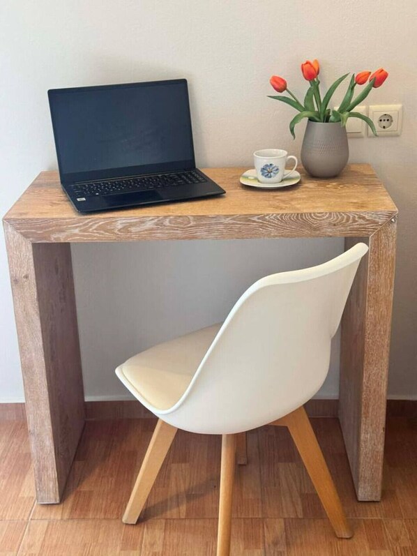 Ein Holztisch mit einem Laptop, einem weißen Stuhl, einer Vase mit Tulpen und einer Tasse.