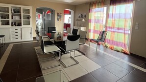 Una sala moderna con comedor, cocina y vista a través de una ventana con cortina colorida.