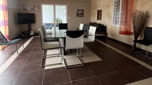 Una sala de estar amplia con comedor, televisor y un gran ventanal con cortinas.