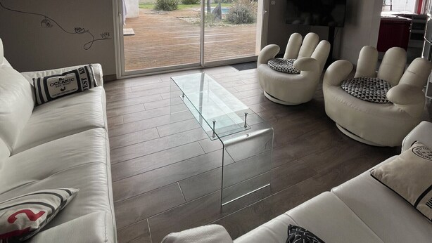 Una sala de estar moderna con una mesa de centro de vidrio, sofás blancos y un televisor.