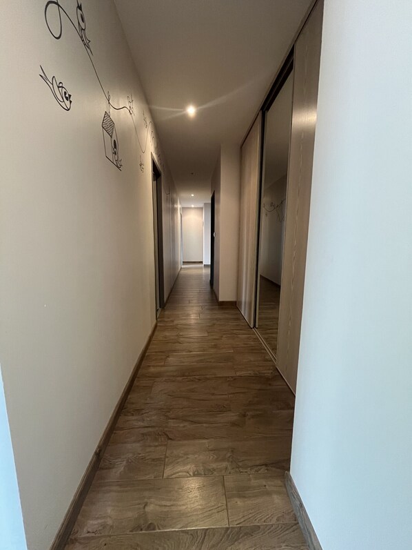 Un pasillo con suelo de madera, paredes blancas y una puerta de armario espejada.