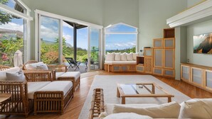 Ein geräumiges Wohnzimmer mit Korbmöbeln, einem Glastisch und Blick ins Freie.