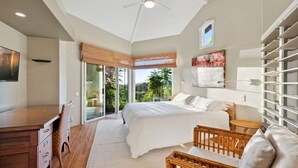 Ein Schlafzimmer mit einem großen Bett, einem Schreibtisch, einem Stuhl, einem kleinen Tisch und Blick ins Grüne durch ein Fenster.