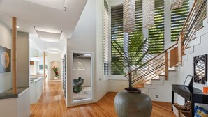 Ein modernes Interieur mit Holzboden, einer großen Vase mit Pflanze, einer Treppe mit Holzhandläufen und einer Wand mit geometrischem Muster.