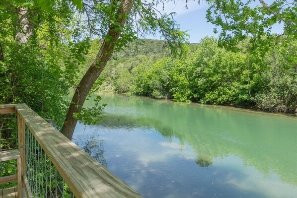 Eine Holzterrasse mit Blick auf einen ruhigen Fluss, umgeben von dichtem Grün.