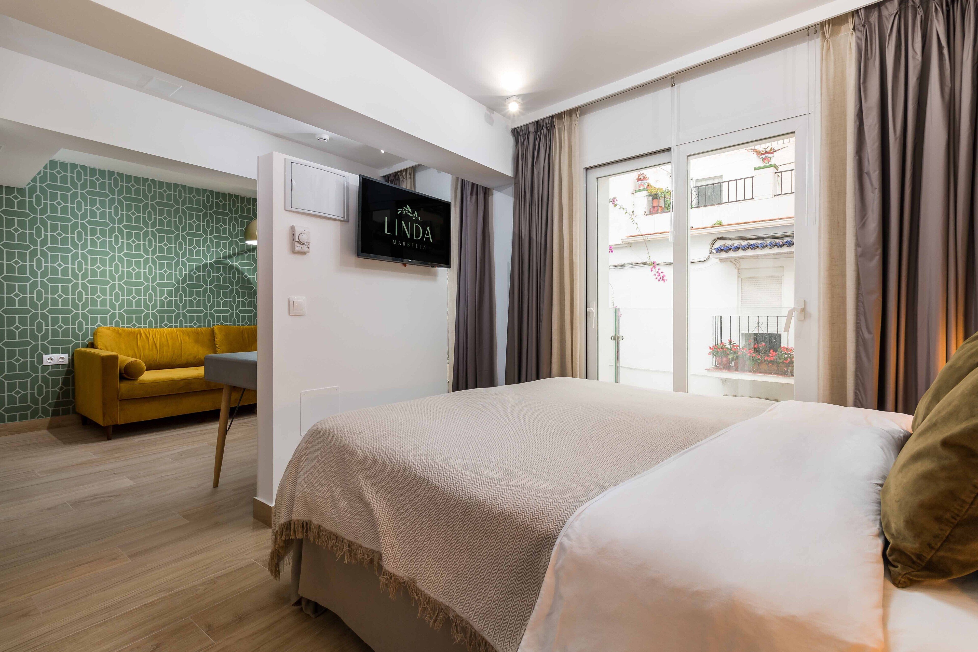 Une chambre d’hôtel avec un lit, un canapé, une télévision et un balcon agrémenté de plantes.