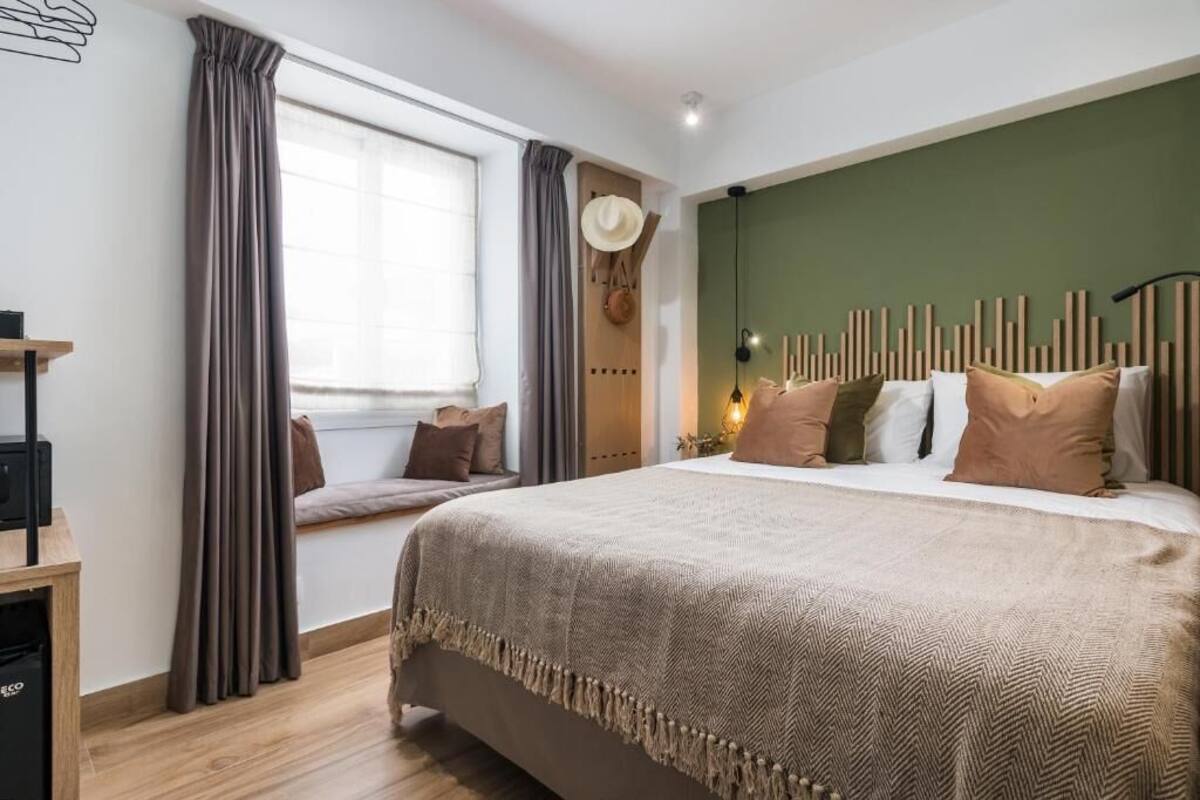 A bedroom with a large bed, a window with curtains, a wall-mounted hat, and a bedside table.