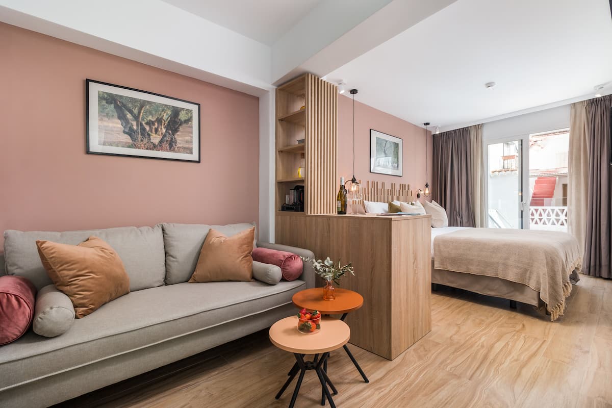 A modern hotel room with a sofa, a small round table, a bed, a wooden cabinet, and a balcony with curtains.