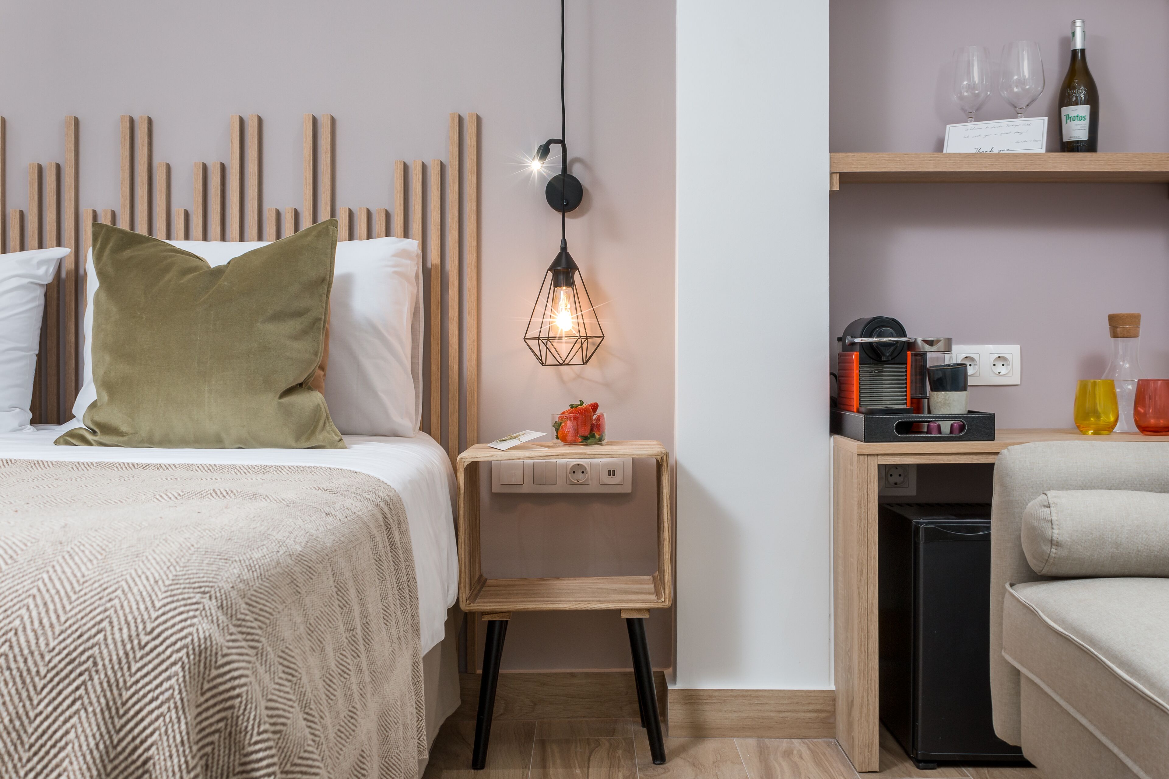 A neatly arranged bedroom with a bed, bedside table, and a small desk with a lamp.