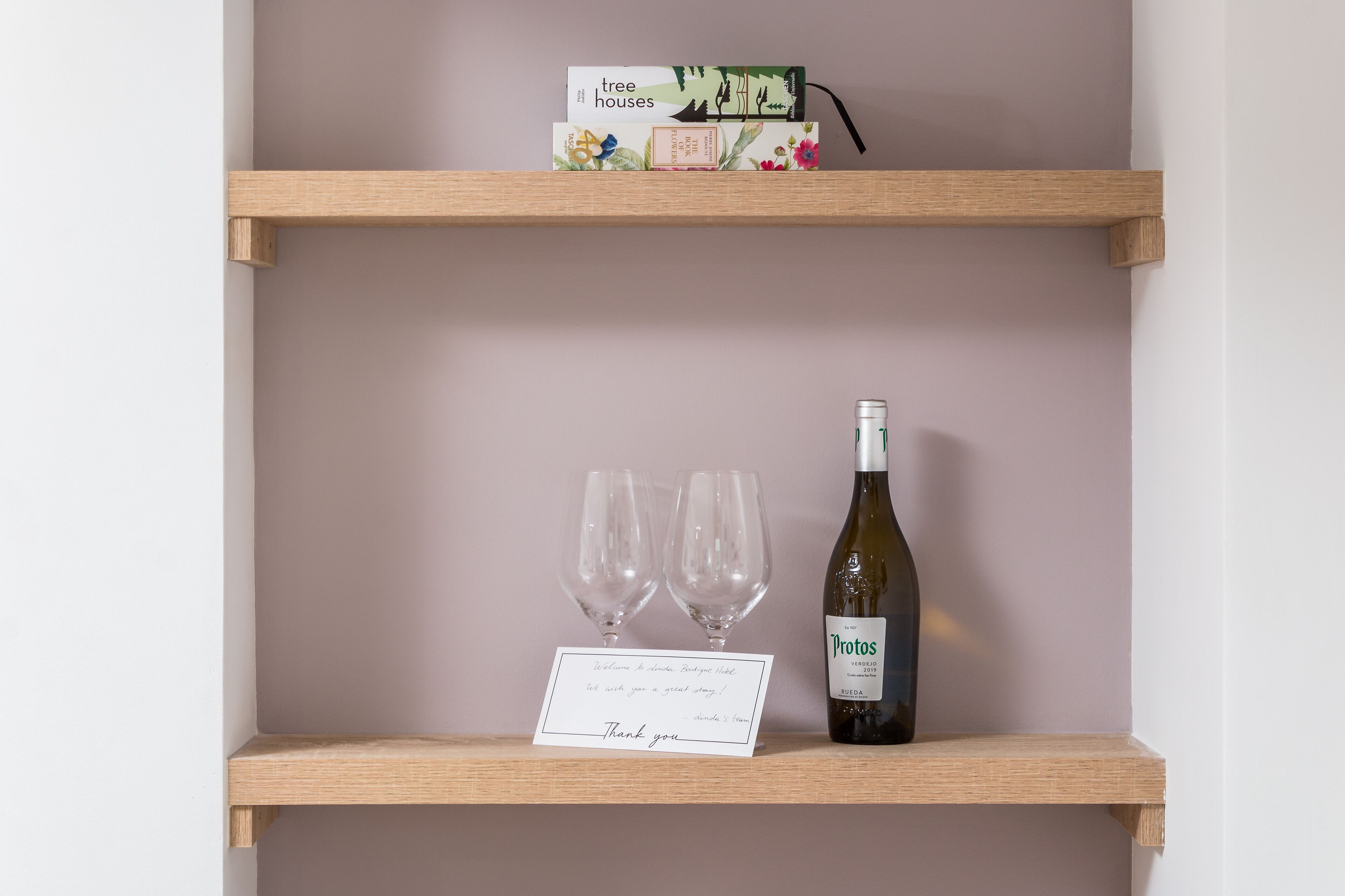 A wooden shelf with a wine bottle and two glasses, a thank you card, and a box labeled "tree houses".