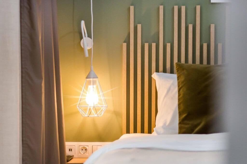A bedroom with a bed, a hanging light fixture, a wooden headboard, and a power outlet.