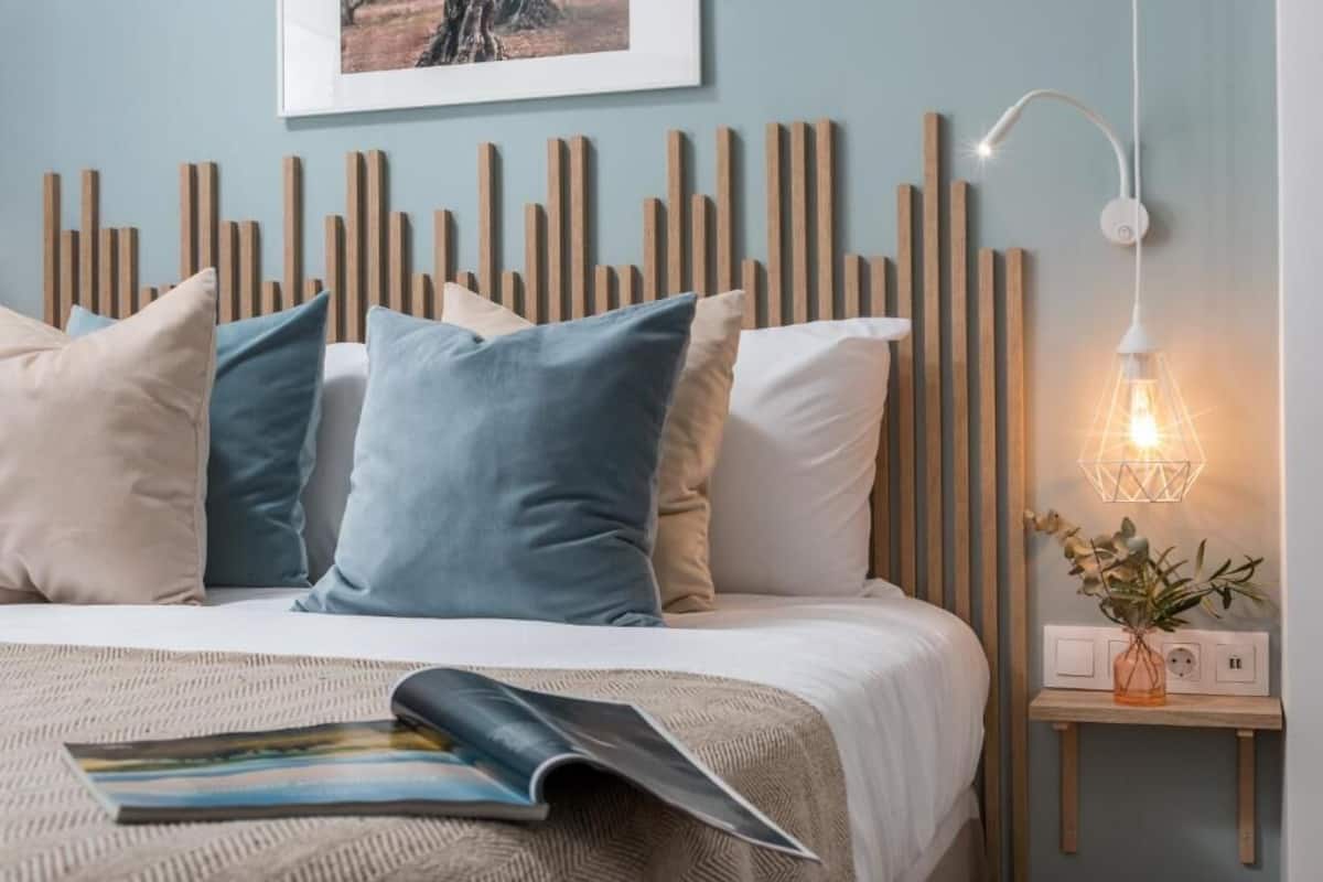 A neatly made bed with a magazine, a wall-mounted picture, and a bedside lamp.