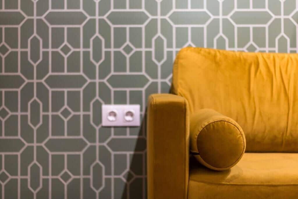 A room with a patterned wallpaper and a mustard-colored sofa.