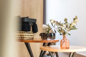 Een rieten mand met een zwarte hoes op een houten tafel, een paar zonnebrillen, en een vaas met bloemen.