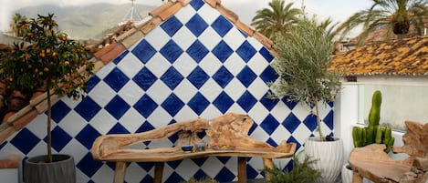 A wooden bench with a rustic design, surrounded by potted plants and a blue and white diamond-patterned wall.
