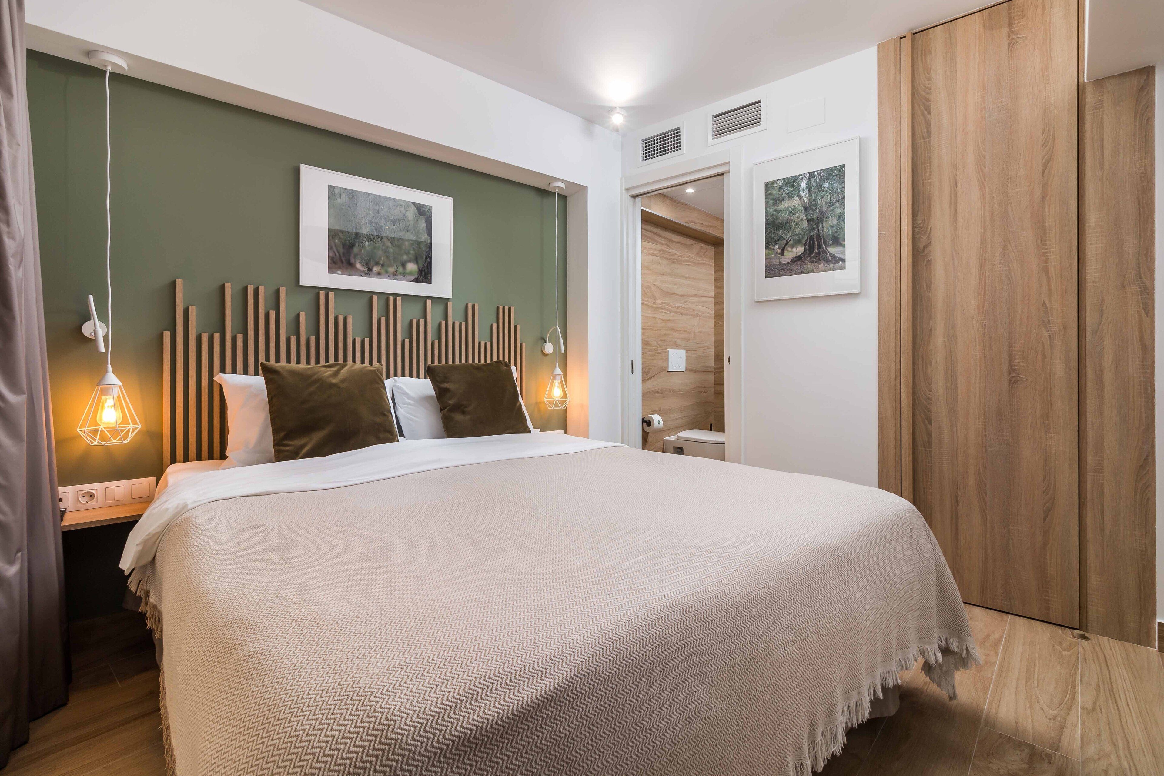 Une chambre à coucher bien rangée, avec un lit, des lampes de chevet, une tête de lit en bois et des tableaux encadrés accrochés au mur.