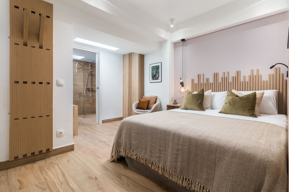 A modern bedroom with a large bed, wooden paneling, a chair, and a shower area.