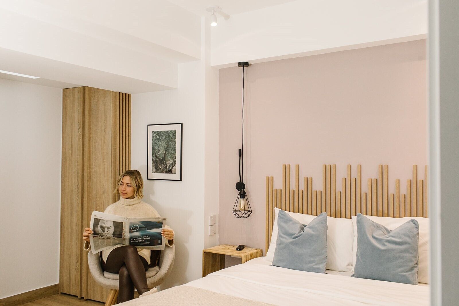 Una habitación de hotel moderna con una cama, un sillón de lectura, una mesita de noche y una lámpara de pared.