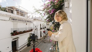 A balcony with a view of a narrow street lined with white buildings, a street lamp, and red poinsettia plants.