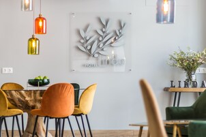 A modern dining area with a wooden table, orange and yellow chairs, and a decorative wall piece.