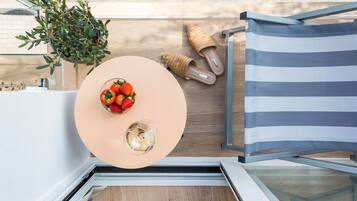Un espacio moderno al aire libre con una mesa redonda, un cuenco de fresas, una copa de vino blanco, una cesta tejida y una silla a rayas.