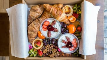 Een doos met croissants, yoghurt met fruit en diverse gebakjes.