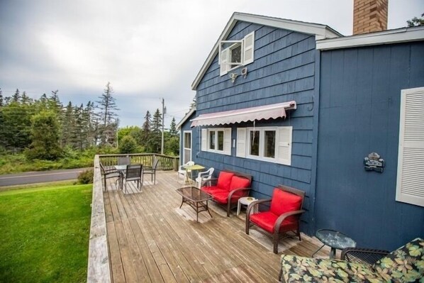 A blue building with a wooden deck, outdoor seating, and a view of the surrounding greenery.