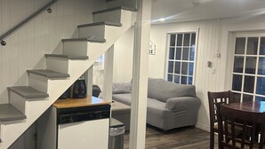 A modern kitchen with a dishwasher, a coffee maker, and a trash can. There is a staircase leading to another level. A dining area with a table and chairs is visible. - Cozy cottage with a hot tub on the bay of fundy (Berwick)
