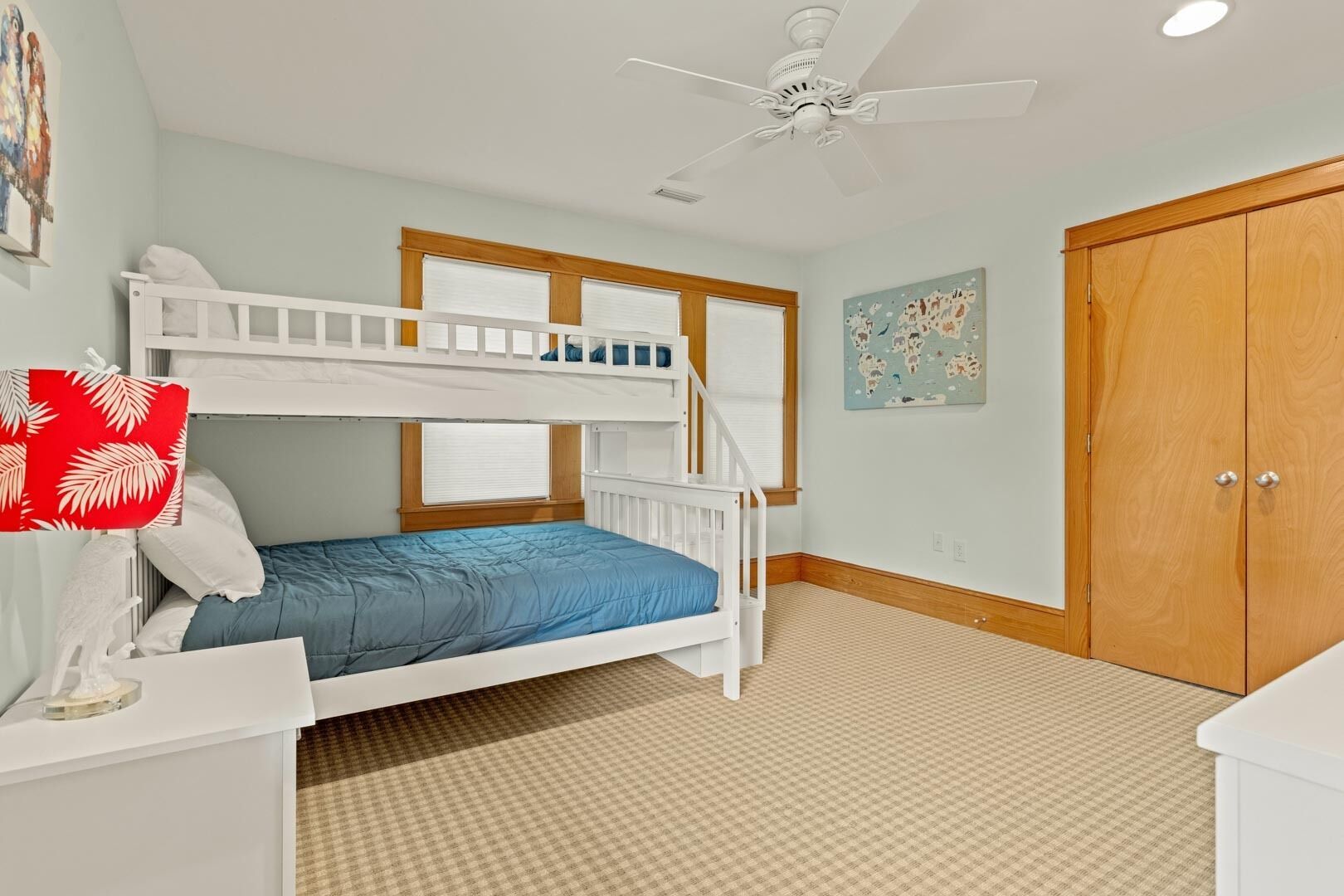 Een kinderkamer met stapelbedden, een plafondventilator, een houten garderobe en een wereldkaart aan de muur.