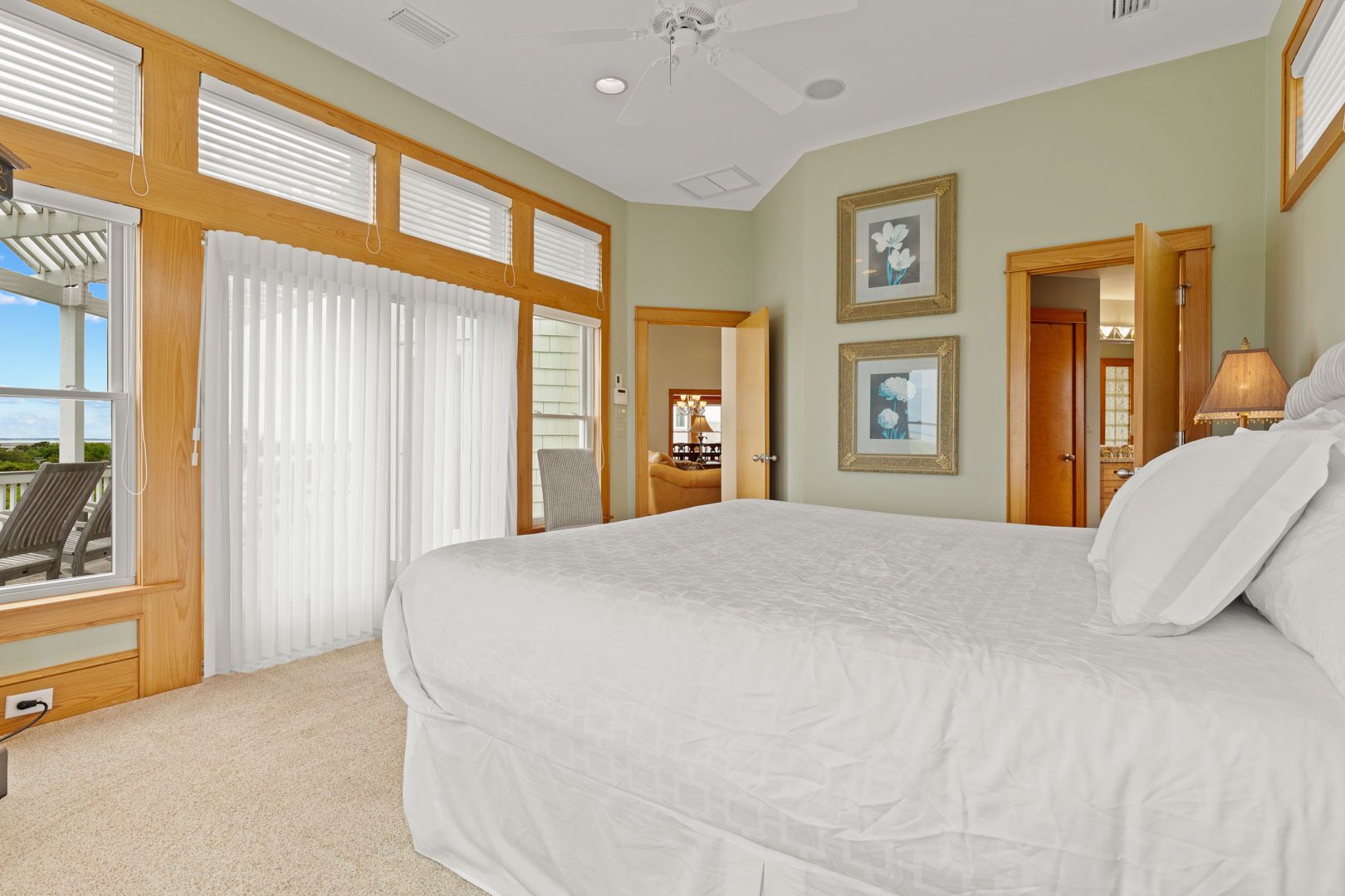 A spacious bedroom with a large bed, wooden ceiling beams, and a view of the outdoors through a sliding glass door.