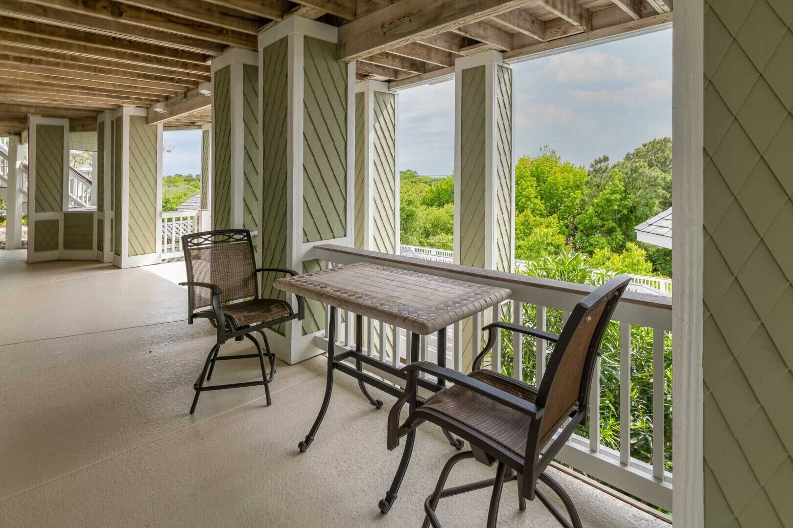 An outdoor patio with a table and two chairs, wooden beams, and a view of greenery.