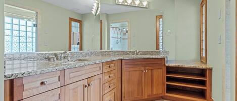 Une salle de bain spacieuse avec un comptoir en granit, des armoires en bois et un grand miroir.