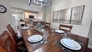 Een eethoek met een lange houten tafel, gedekt voor vier personen, omringd door houten stoelen. Achtergrond is een zichtbare keuken.