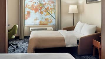 A hotel room with a bed, a chair, a desk, a lamp, and a window with a view of autumn leaves.